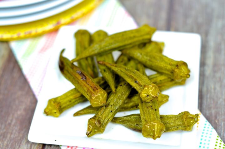 Air fryer okra served on a white plate on top a polka dot napkin on a grey table. 