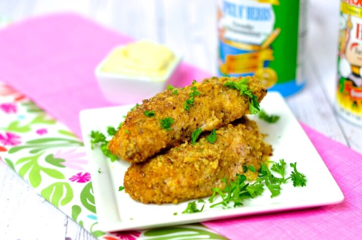 Air fryer chicken tenders on a white plate placed on a pink and green napkin on a white table. 