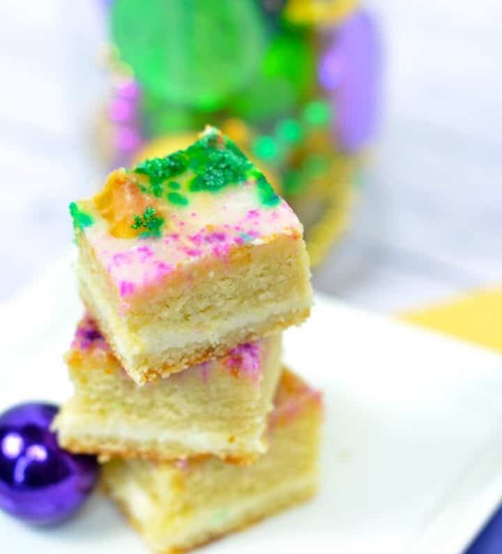 3 small slices of king cake served on a white plate on top of a yellow, green, and purple napkin.