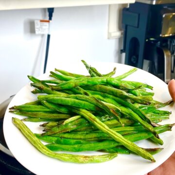 air fried green beans served in a white plate held by a hand