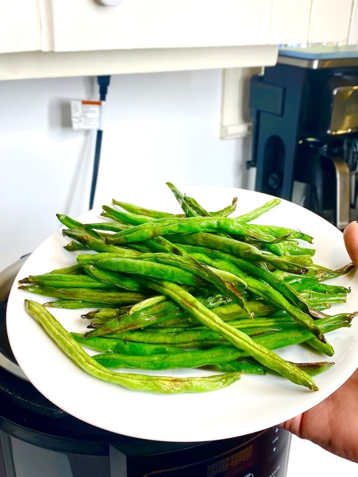 air fried green beans served in a white plate held by a hand