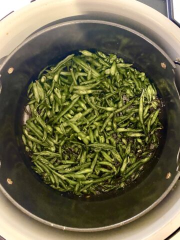 Cooked frozen green beans in the air fryer basket of a ninja foodi.