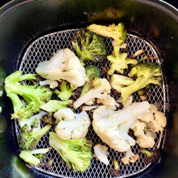 Cooked air fryer broccoli and cauliflower in an air fryer basket