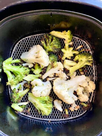 Cooked air fryer broccoli and cauliflower in an air fryer basket