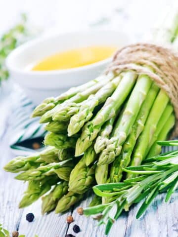 bundle of asparagus wrapped in decorative rope. The bundle of asparagus is sitting on a white table.