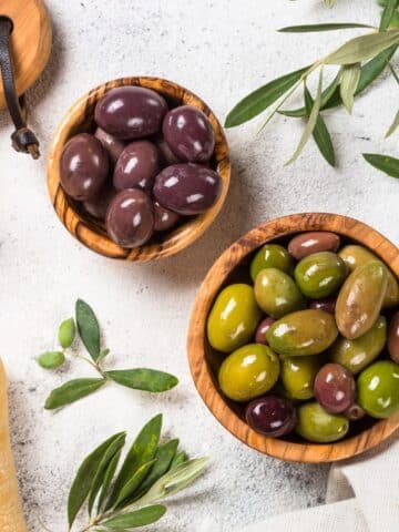 1 bowl of green olives, 1 bowl of black olives sitting on a white table.